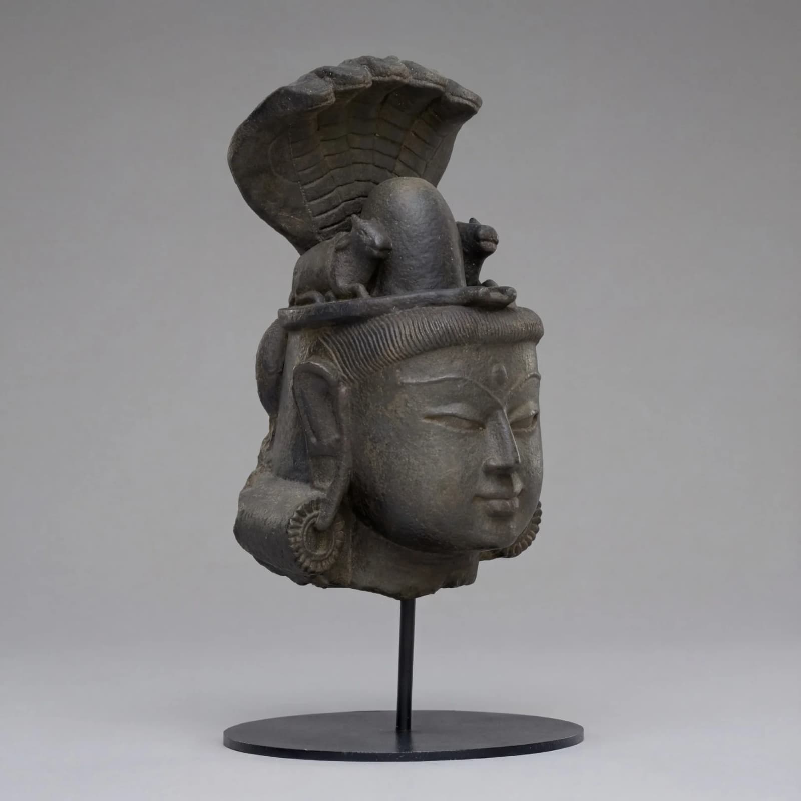 A three-quarter view of the Shiva Lingam with Nandi & Serpent stone composite replica, showcasing intricate carved facial features.
