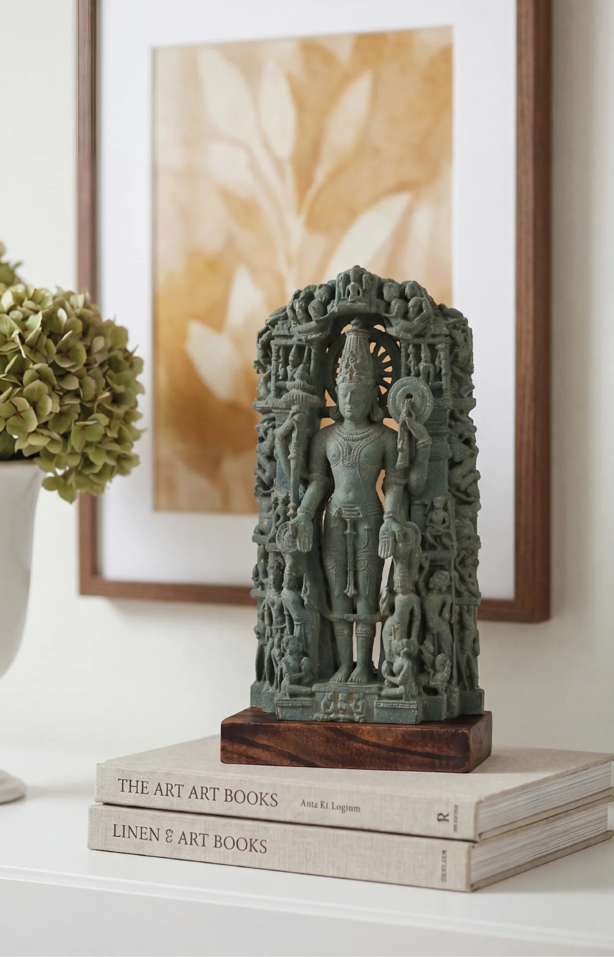 A Chaturbhuj Vishnu Sculpture museum replica in stone composite, displayed on stacked books in a serene home interior setting.
