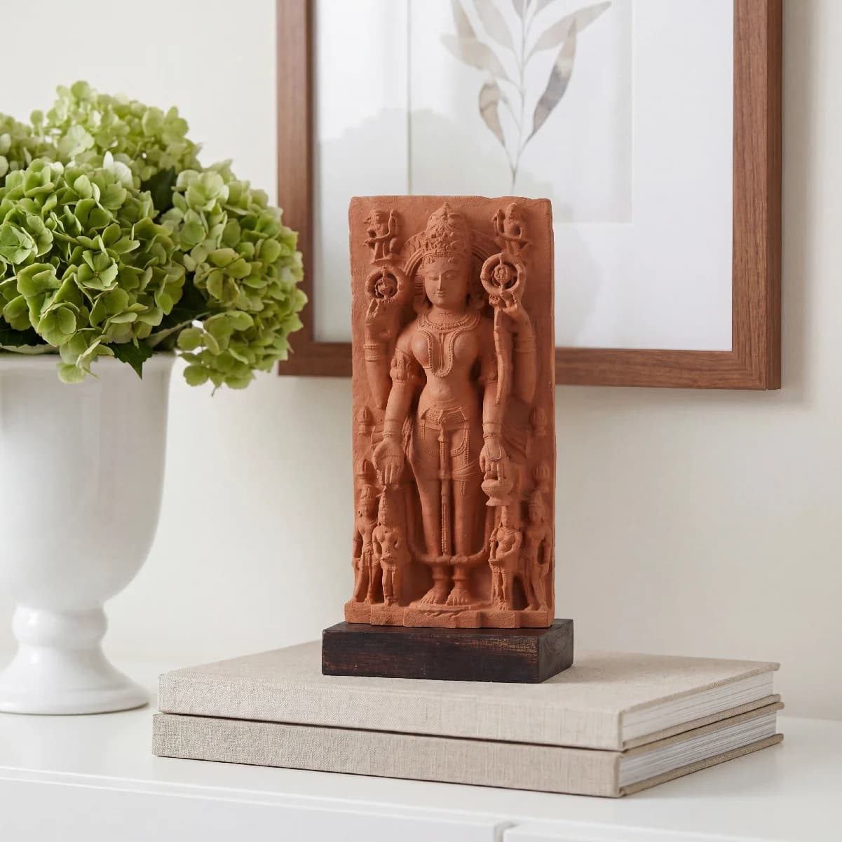 A Gauri Parvati Sculpture museum replica made of stone composite, displayed on a stack of books next to green flowers.