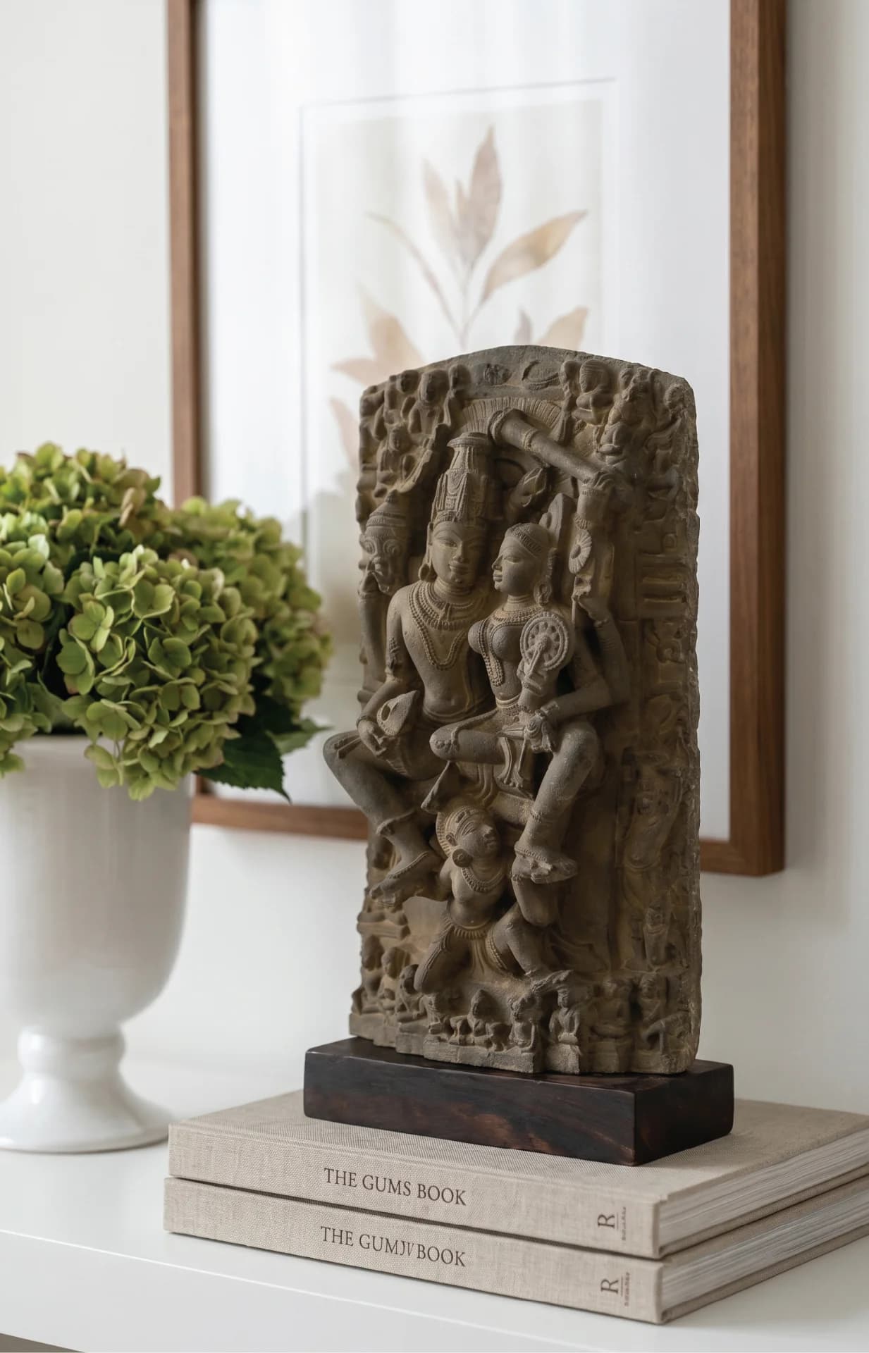 A stone composite Lakshmi Narayan Sculpture displayed on a stack of books next to a white vase.
