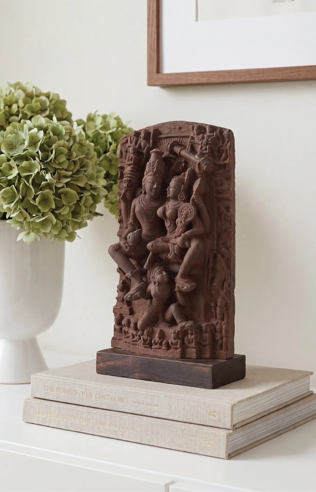 The Lakshmi Narayan Sculpture displayed on a stack of books next to a vase of green flowers.