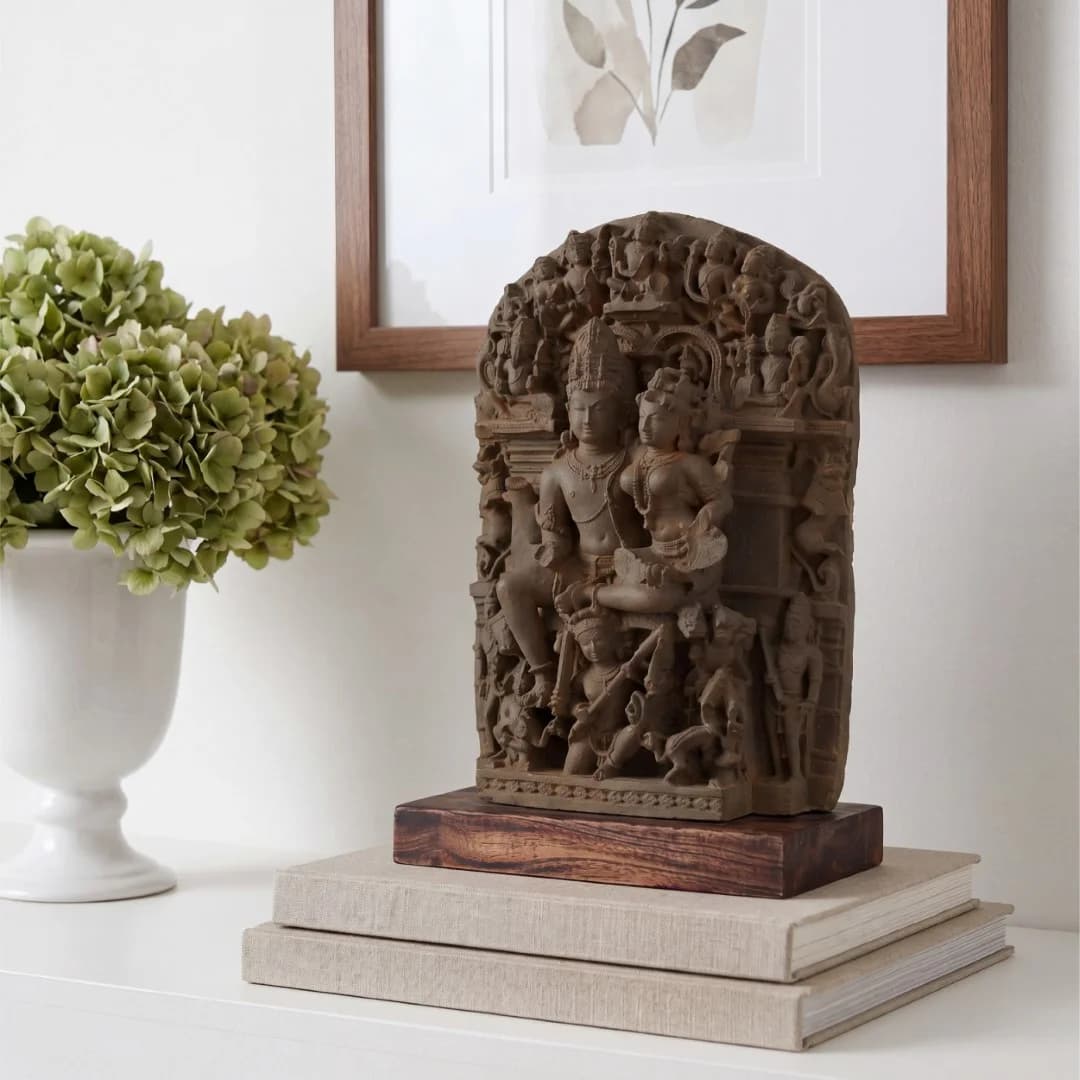 The Ravananugraha Sculpture, a stone composite museum replica, sits on a teak base atop books in a home setting.
